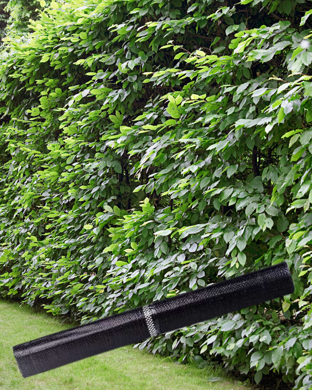 Attrezzo da giardino nero adagiato sull'erba con una siepe verde sullo sfondo.